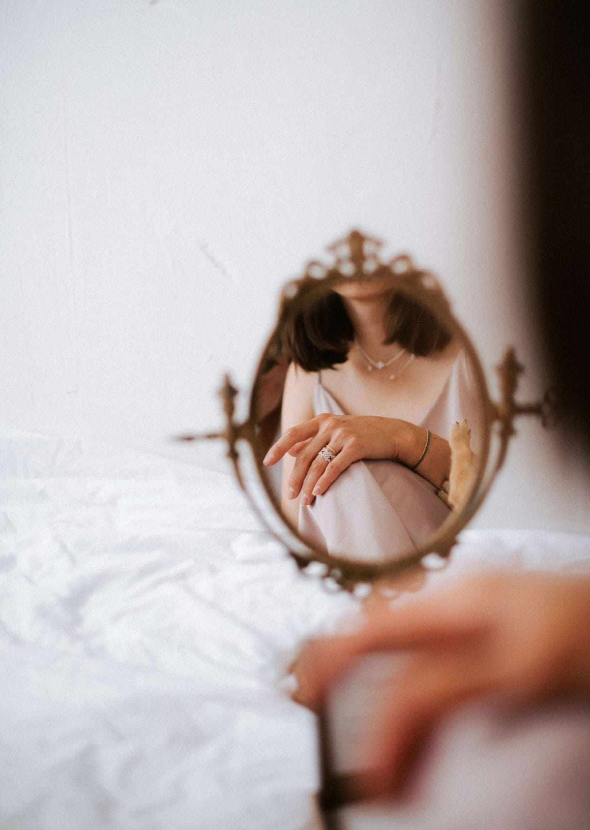 Woman reflected in antique mirror wearing silk slip dress and jewelry
